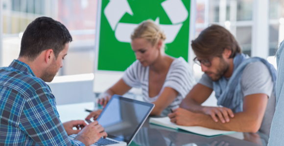 Drei Personen sitzen an einem Tisch und arbeiten; im Hintergrund sieht man das Recycling-Zeichen - drei Pfeile, die ein Dreieck bilden