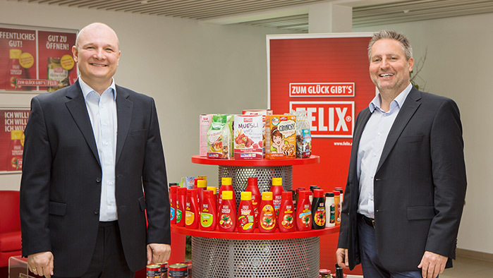 zwei Personen im Anzug stehen vor einem Produktregal gefüllt mit FELIX-Produkten
