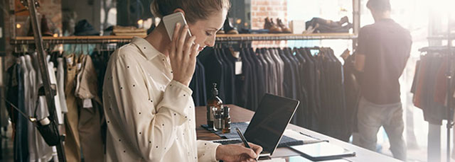 Verkäuferin in einem Kleidershop telefoniert mit Smartphone