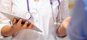 Frau in Arztkittel und mit Stethoskop und Tablet in der Hand symbolisiert die spezifischen Telekommunikations- und Software-Lösungen für Aerzte, Apotheken und das Gesundheitswesen.